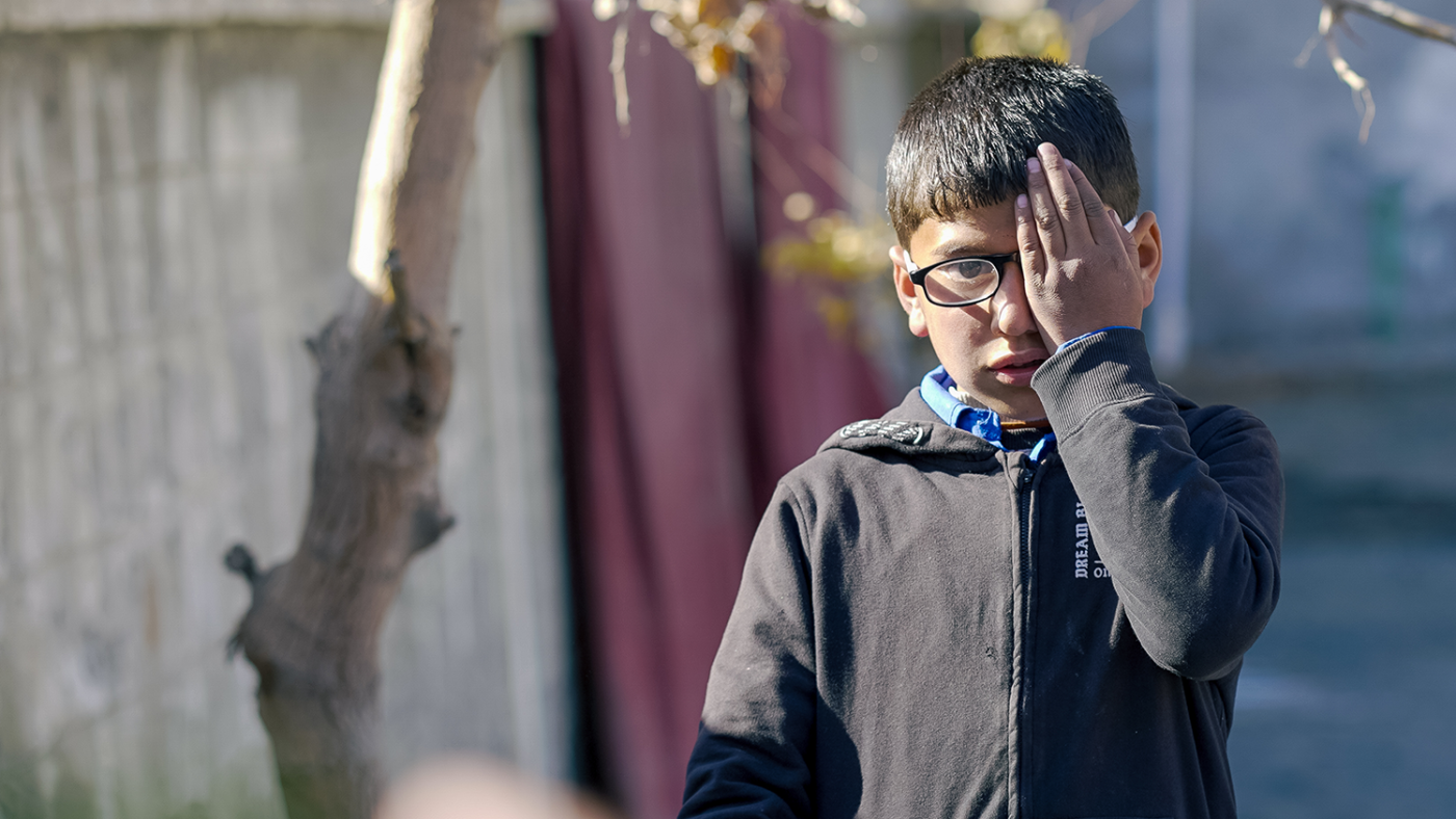 A boy wearing a pair of glasses covers his left eye with his hand.