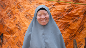 Saudat, wearing a grey hijab, smiles broadly.